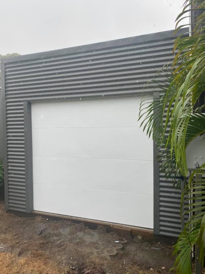 A white garage door is sitting next to a palm tree.