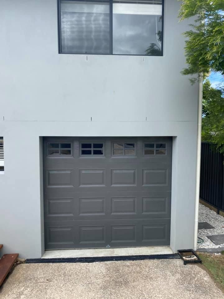 A gray garage door is on the side of a white house.