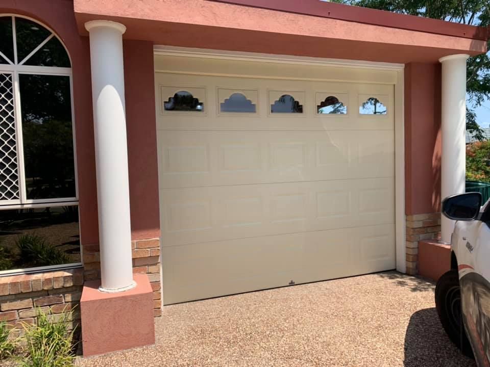 A white car is parked in front of a white garage door.