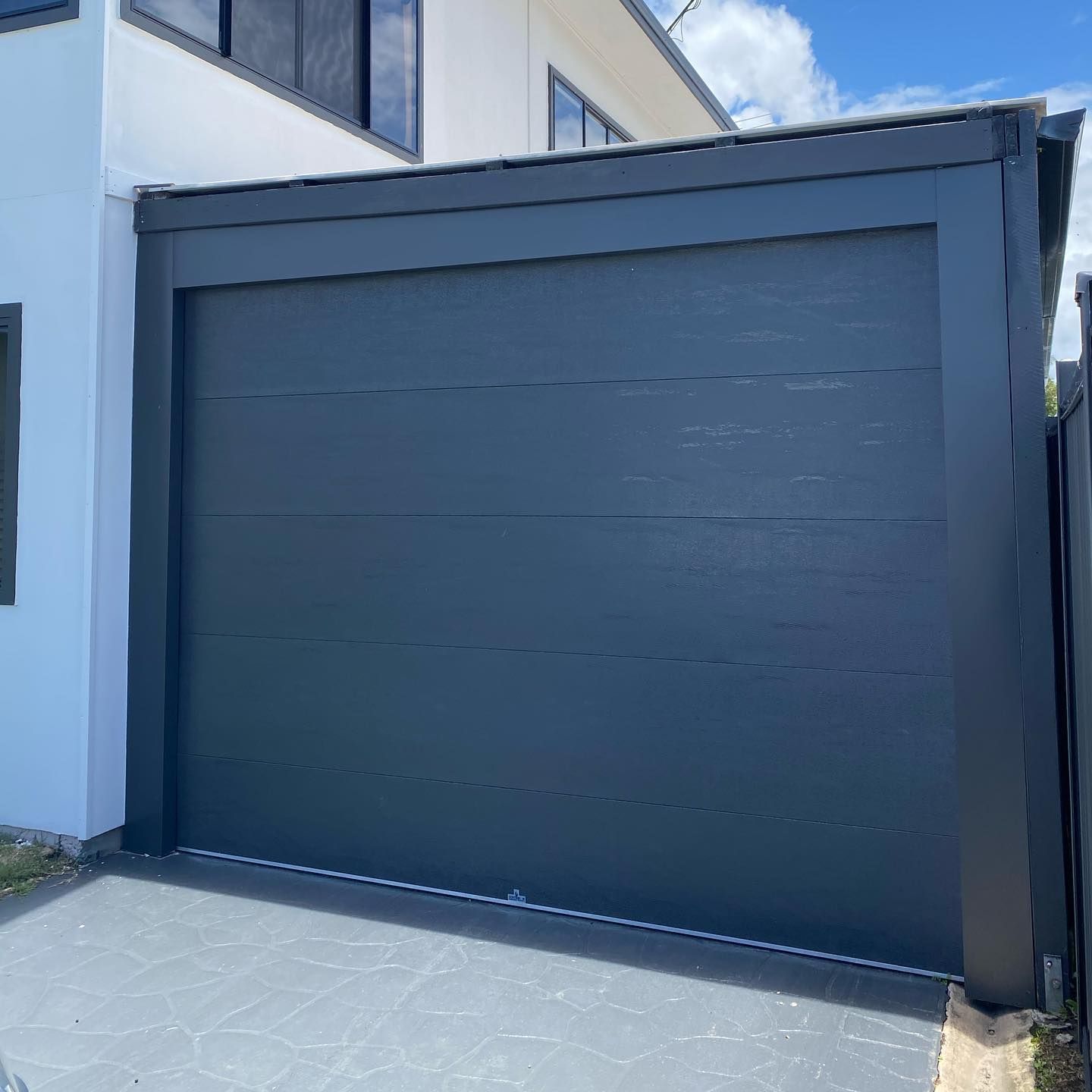 A black garage door is sitting in front of a white house.