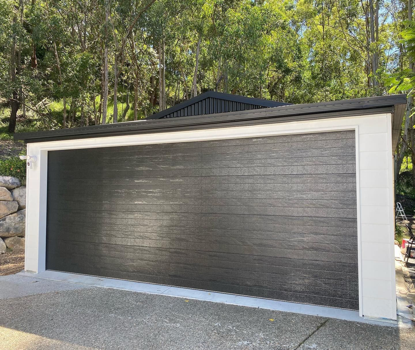 A black and white garage door is sitting in front of a forest.