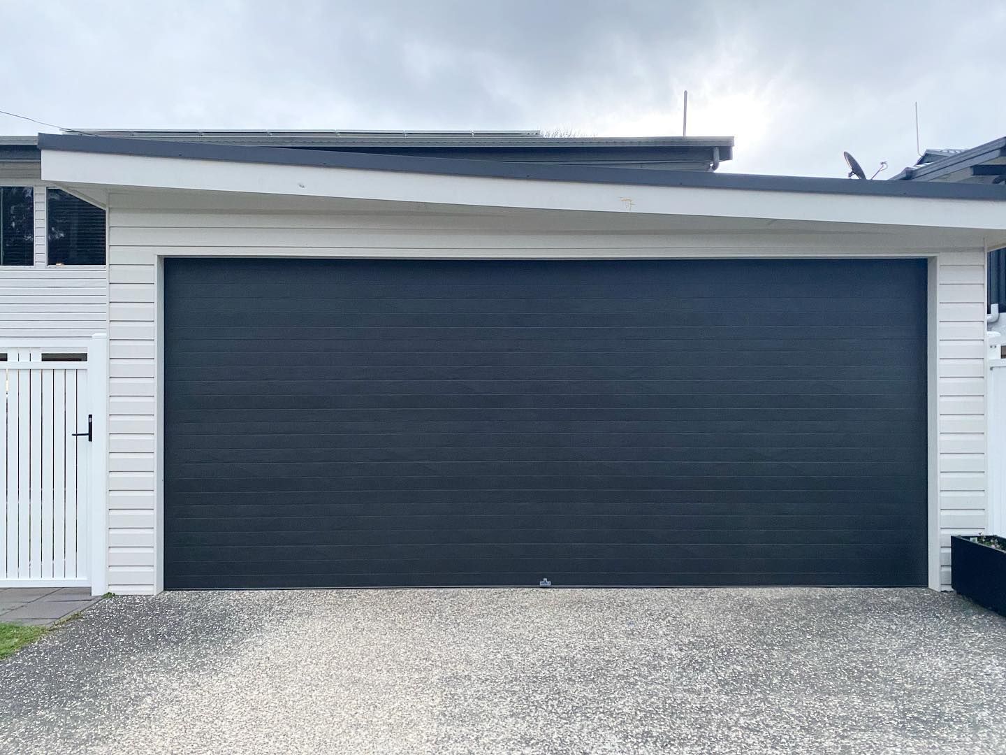 A black garage door is sitting in front of a white house.