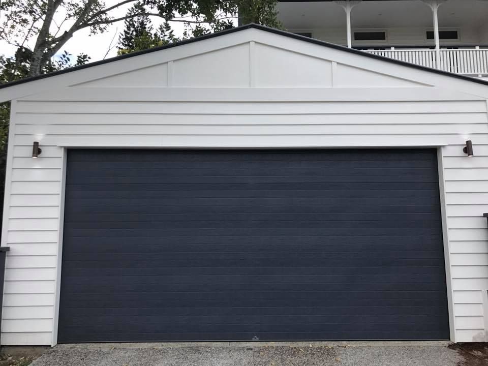 A white garage with a black garage door is next to a house.