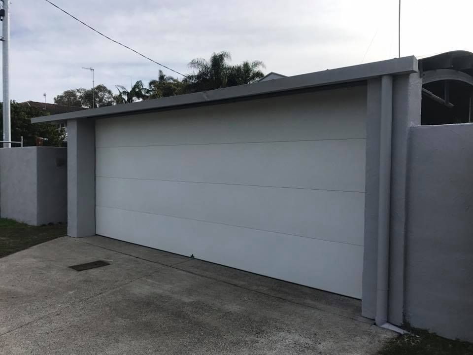 A white garage door is sitting next to a concrete wall.