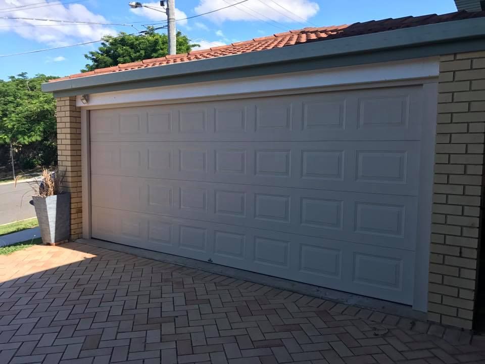 A white garage door is sitting in front of a brick building.