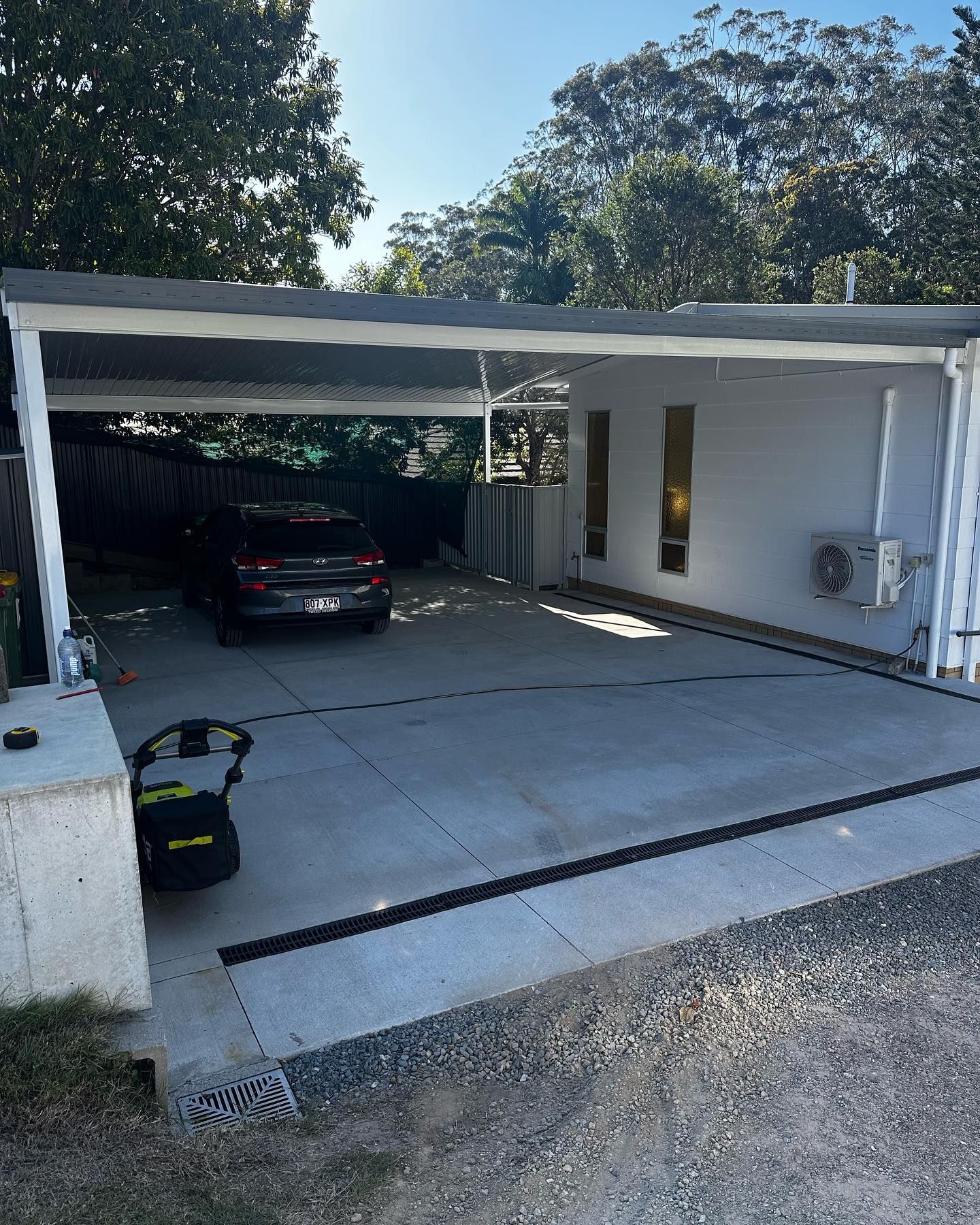 A car is parked under a canopy in a driveway.