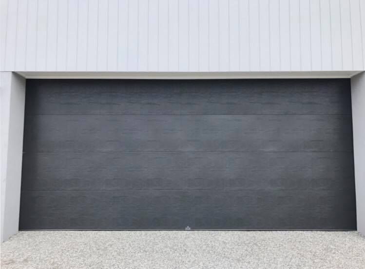 A black garage door is sitting in front of a white building.