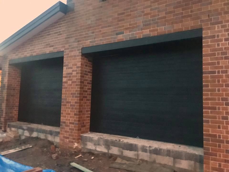 A brick building with two black garage doors is being built.