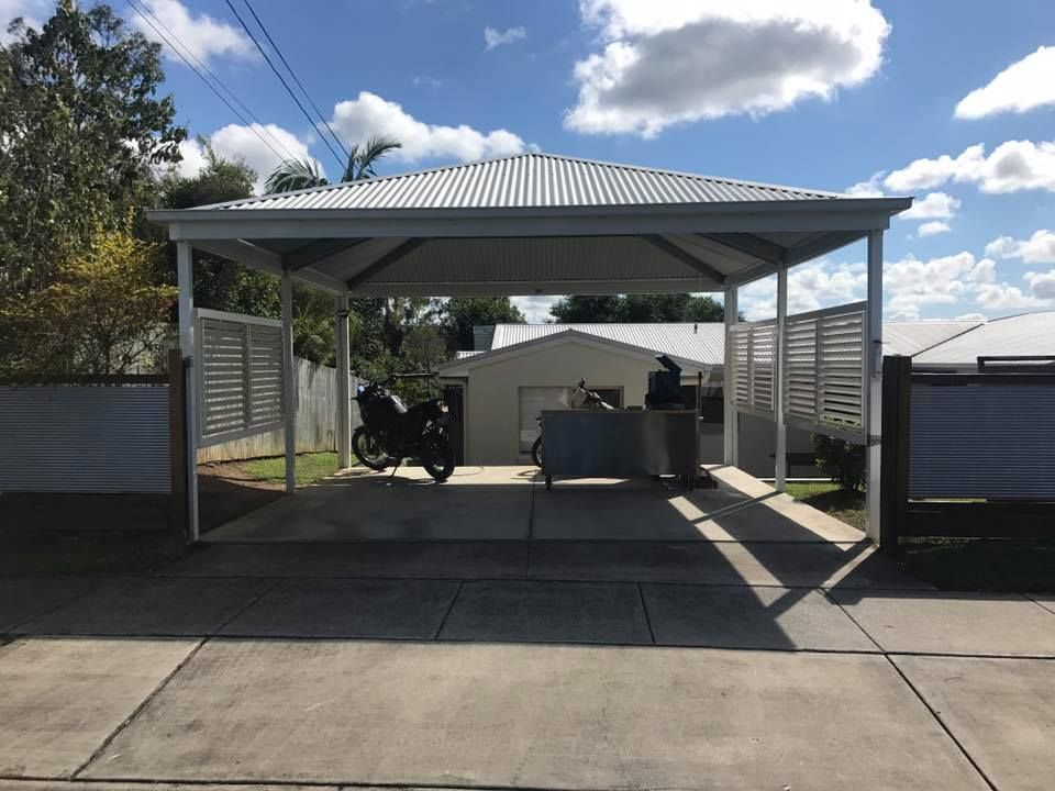 A motorcycle is parked under a carport in front of a house.