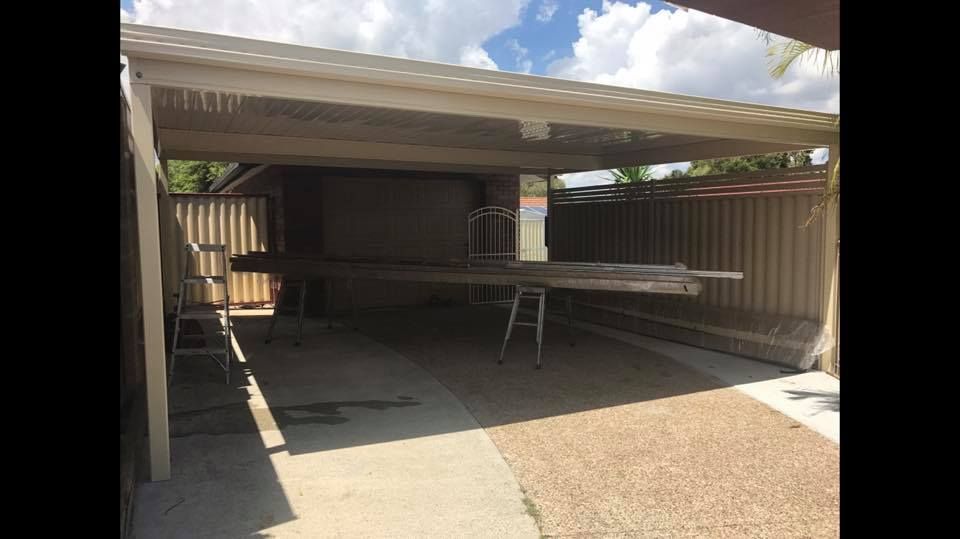 A carport with a table underneath it and a ladder.