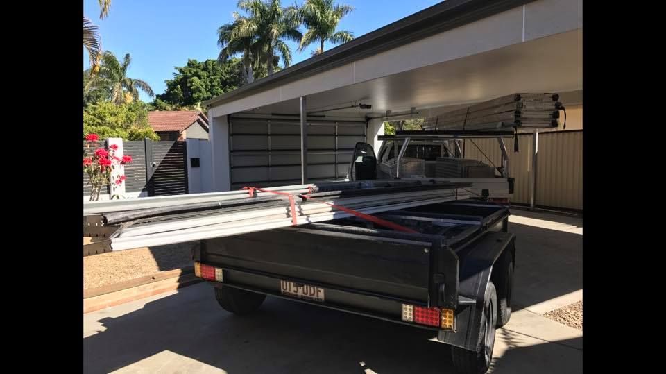 A trailer is parked under a garage door next to a house.