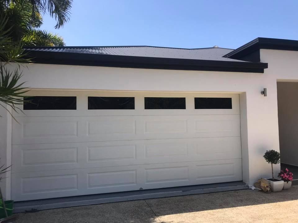 A white garage door with black windows is sitting in front of a white house.