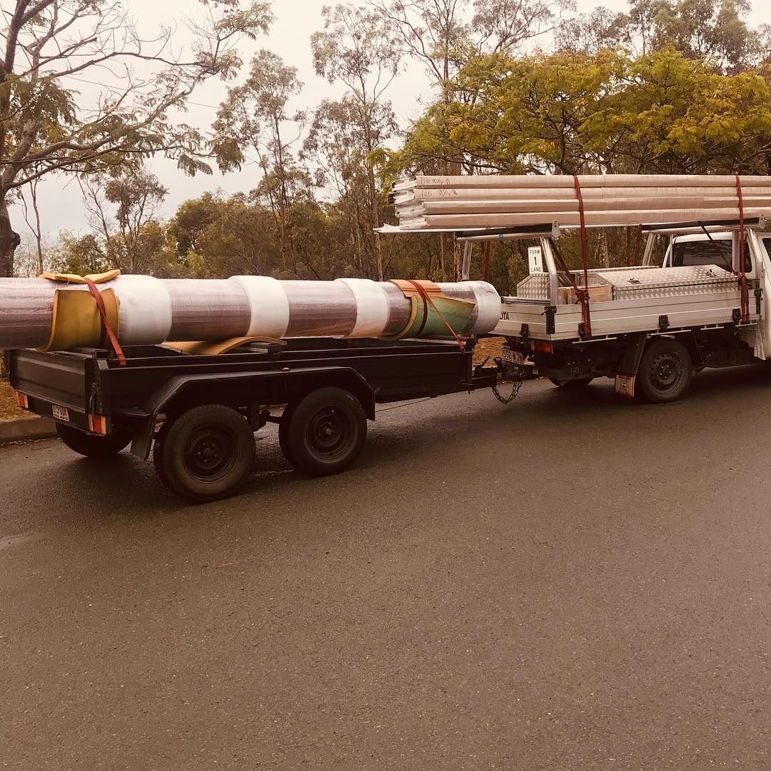 A truck is pulling a trailer with pipes on it