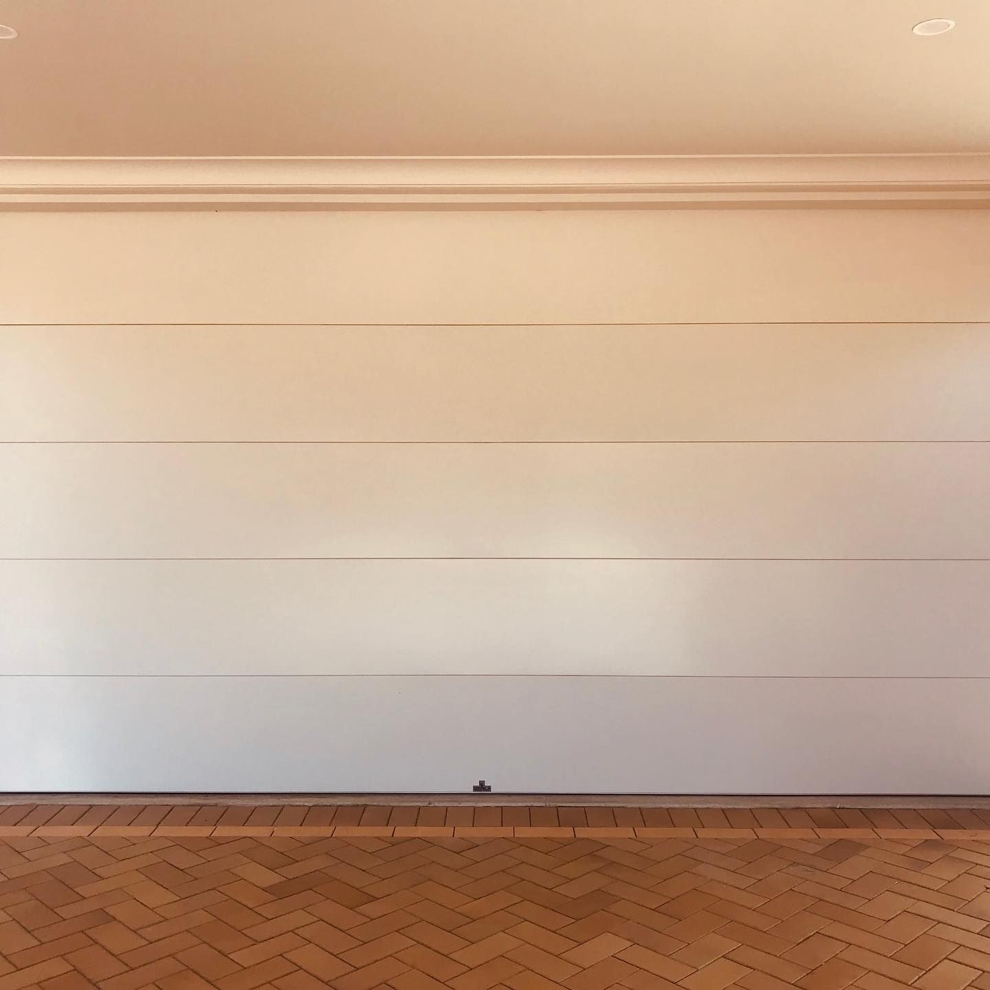 An empty garage with a white garage door and a wooden floor.