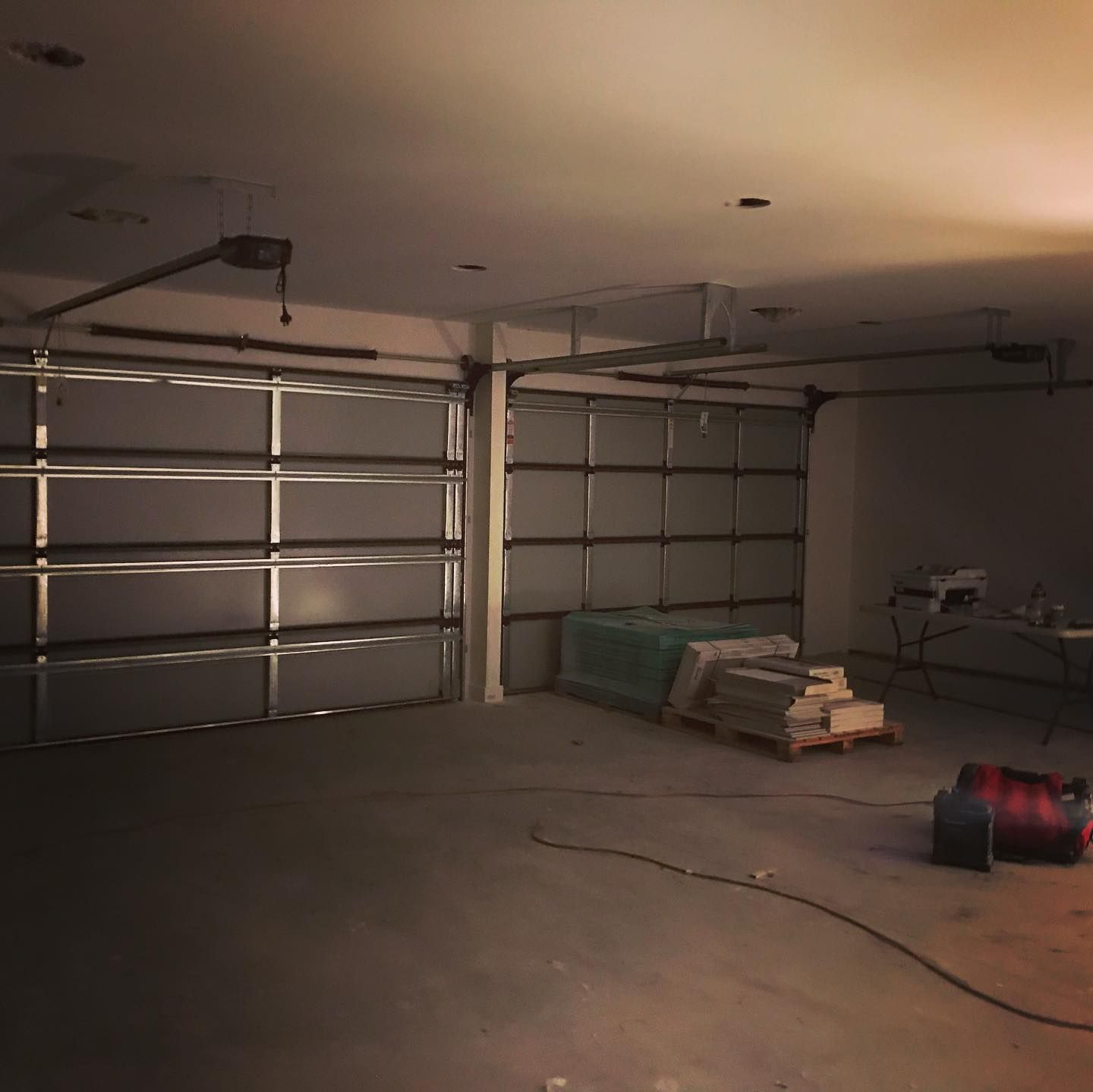An empty garage with a garage door open and a stack of tiles on the floor.