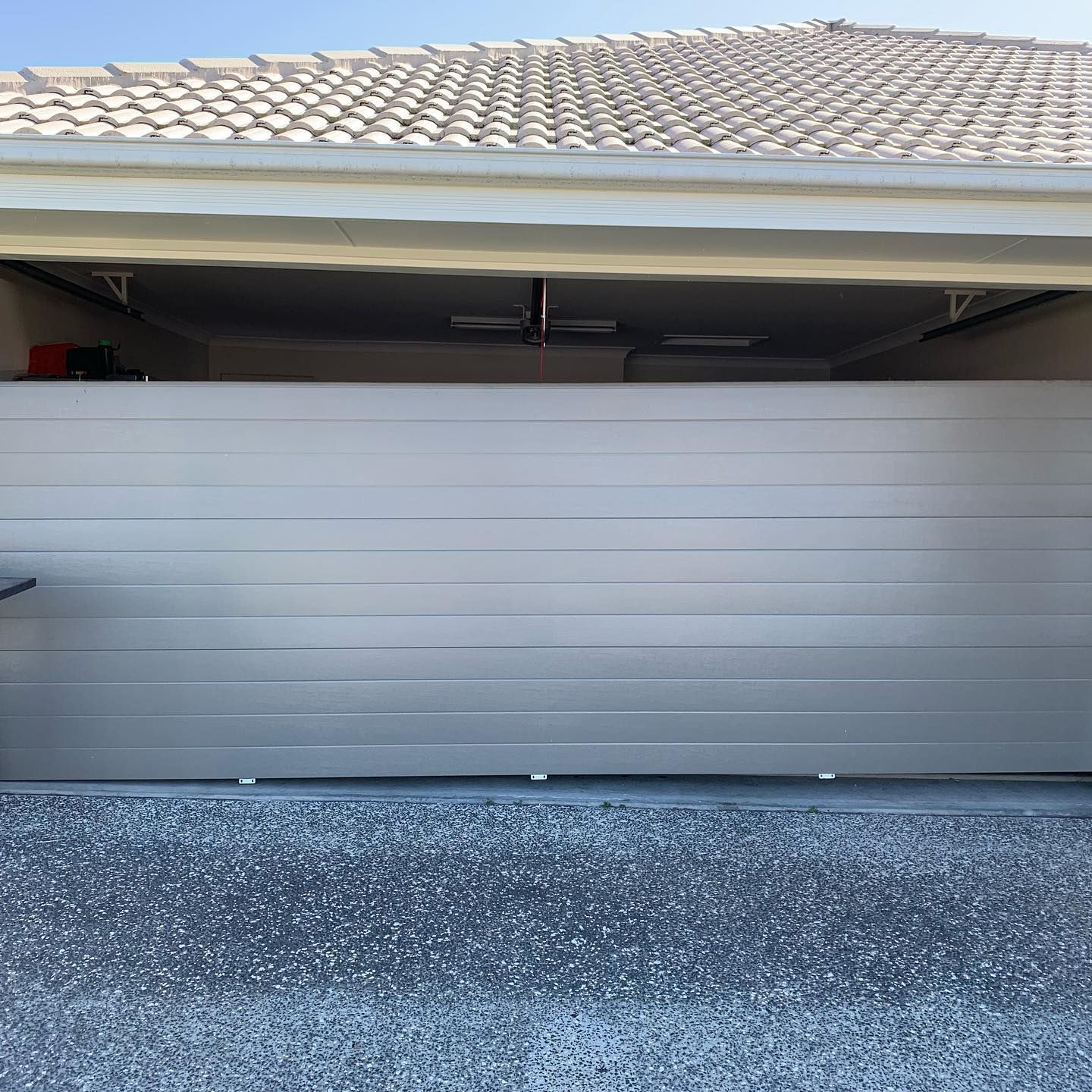 A garage door is open to a house with a tiled roof.
