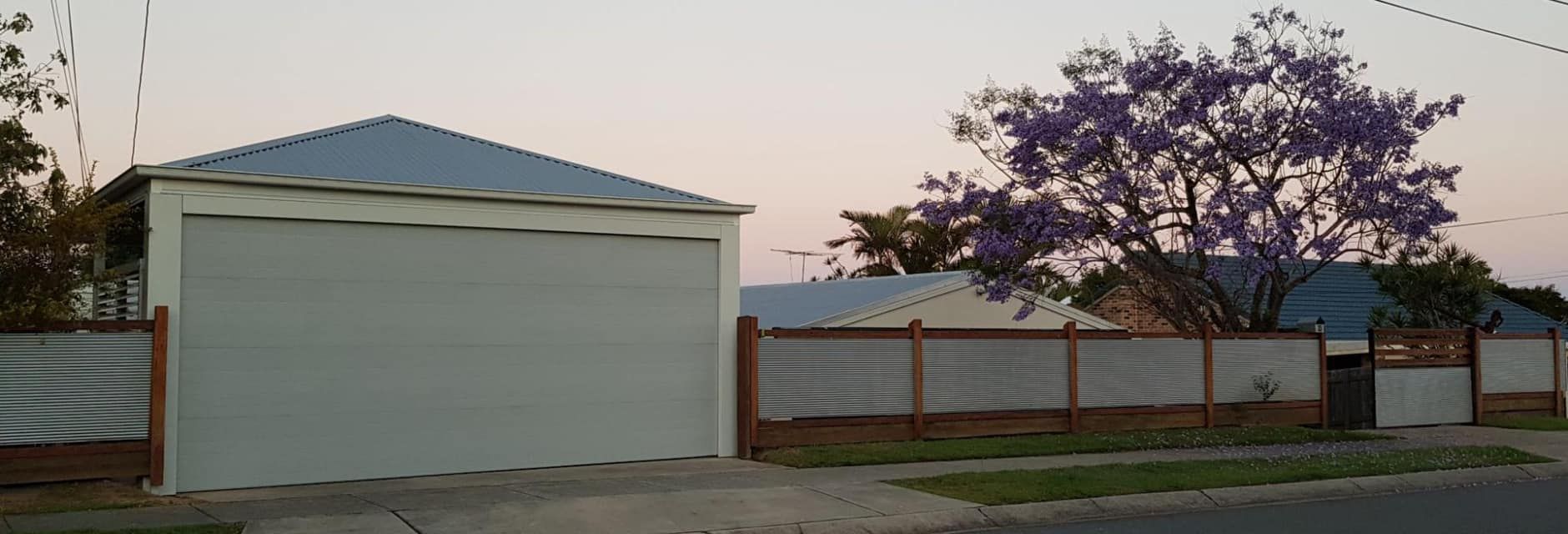 A white garage with a blue roof and a purple tree in the background.