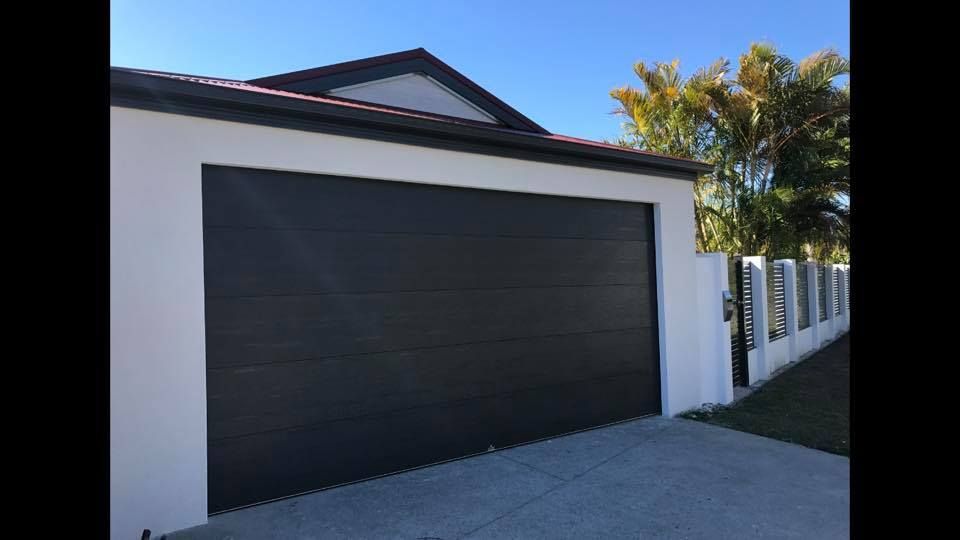 A black garage door is sitting in front of a white house.