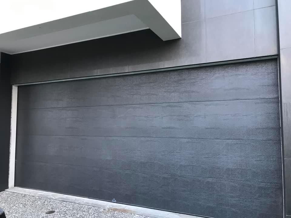 A black garage door is sitting on the side of a building.