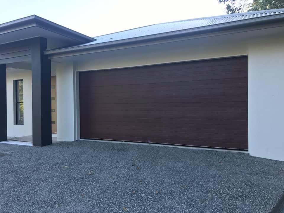 A large brown garage door is sitting in front of a white house.