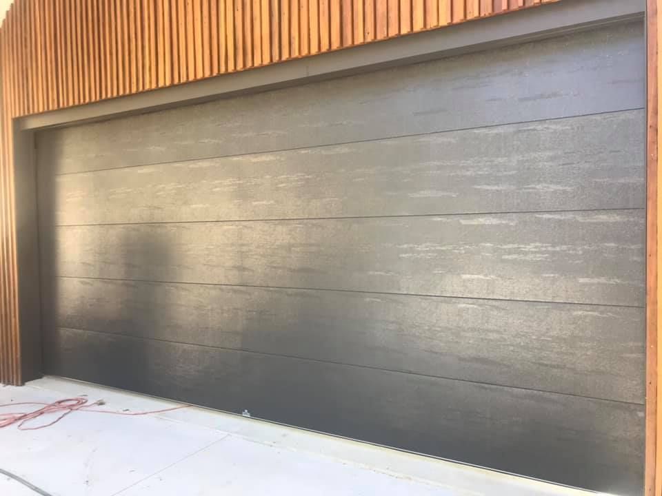 A black garage door with a wooden siding on the side of a building.