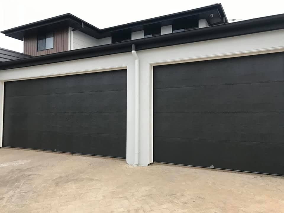 There are two black garage doors on the side of a house.