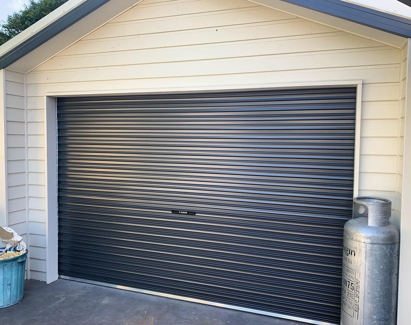 A black garage door is open next to a gas cylinder.