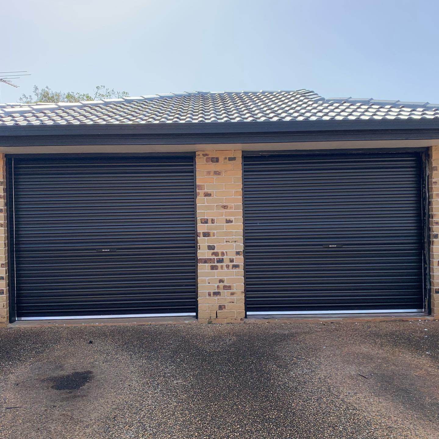 A garage with two black garage doors and a brick wall.