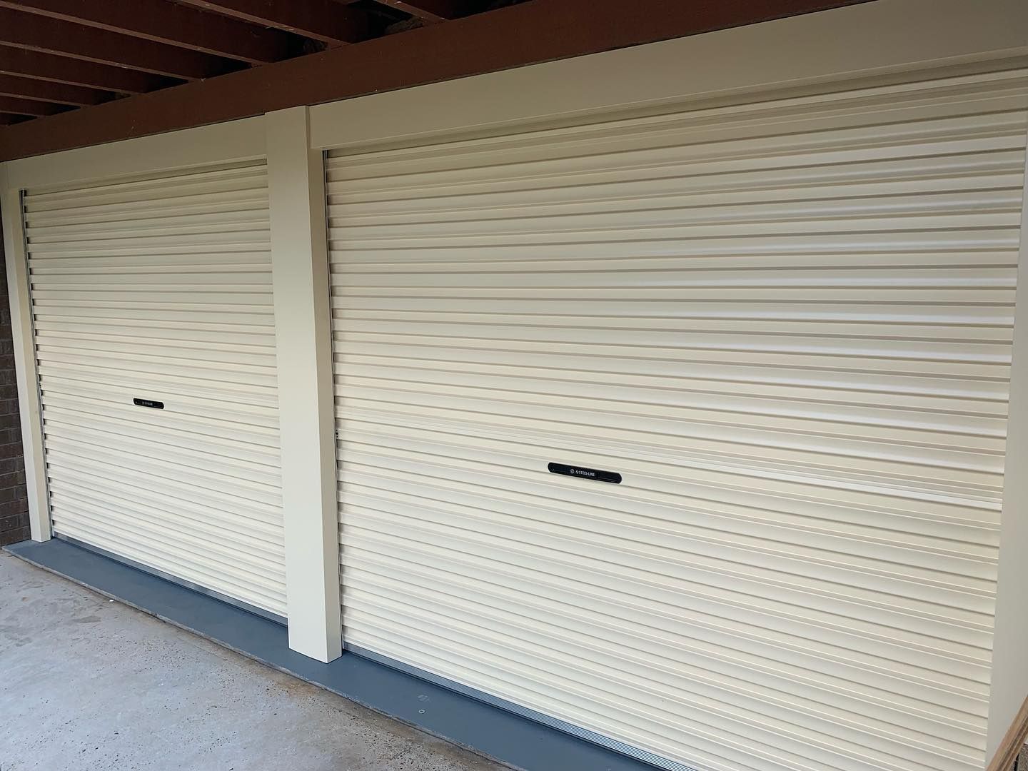 Two white garage doors are sitting next to each other under a roof.