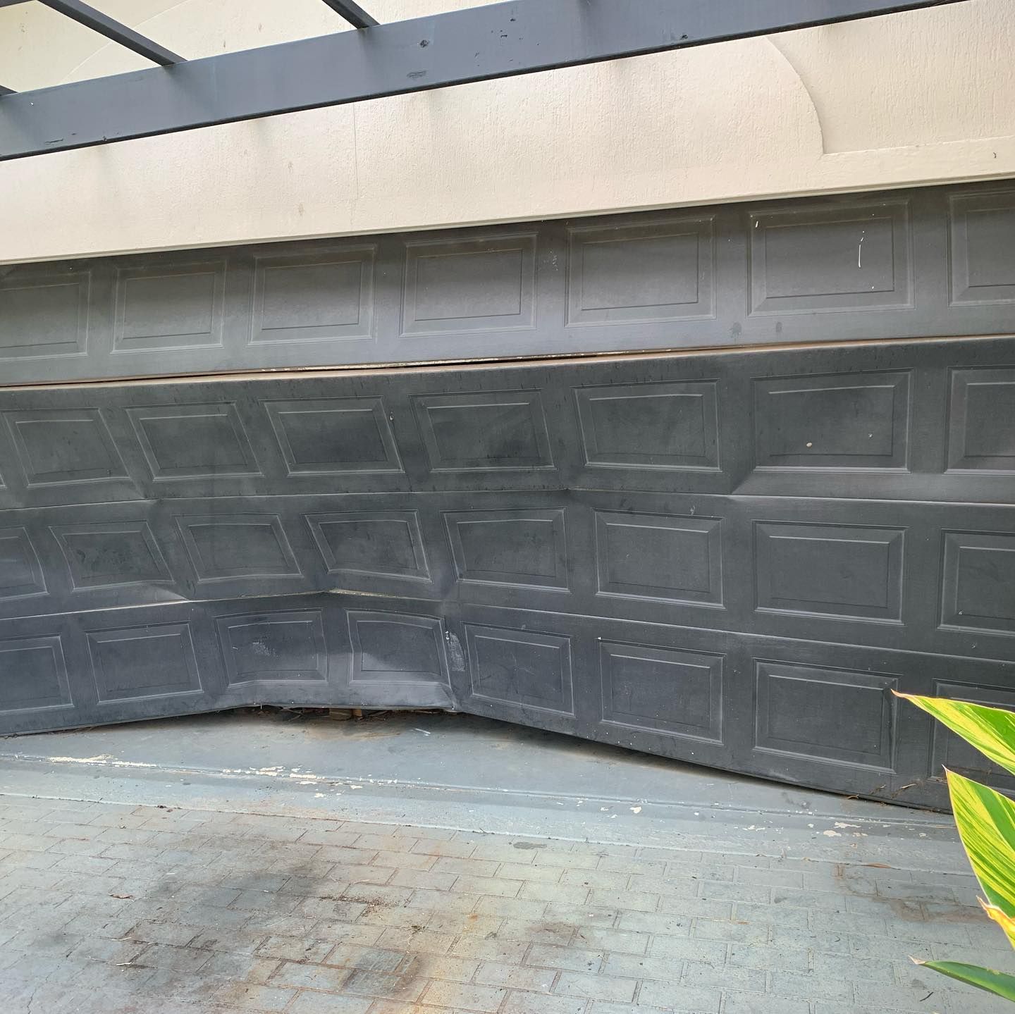 A broken garage door is sitting on a brick driveway next to a plant.