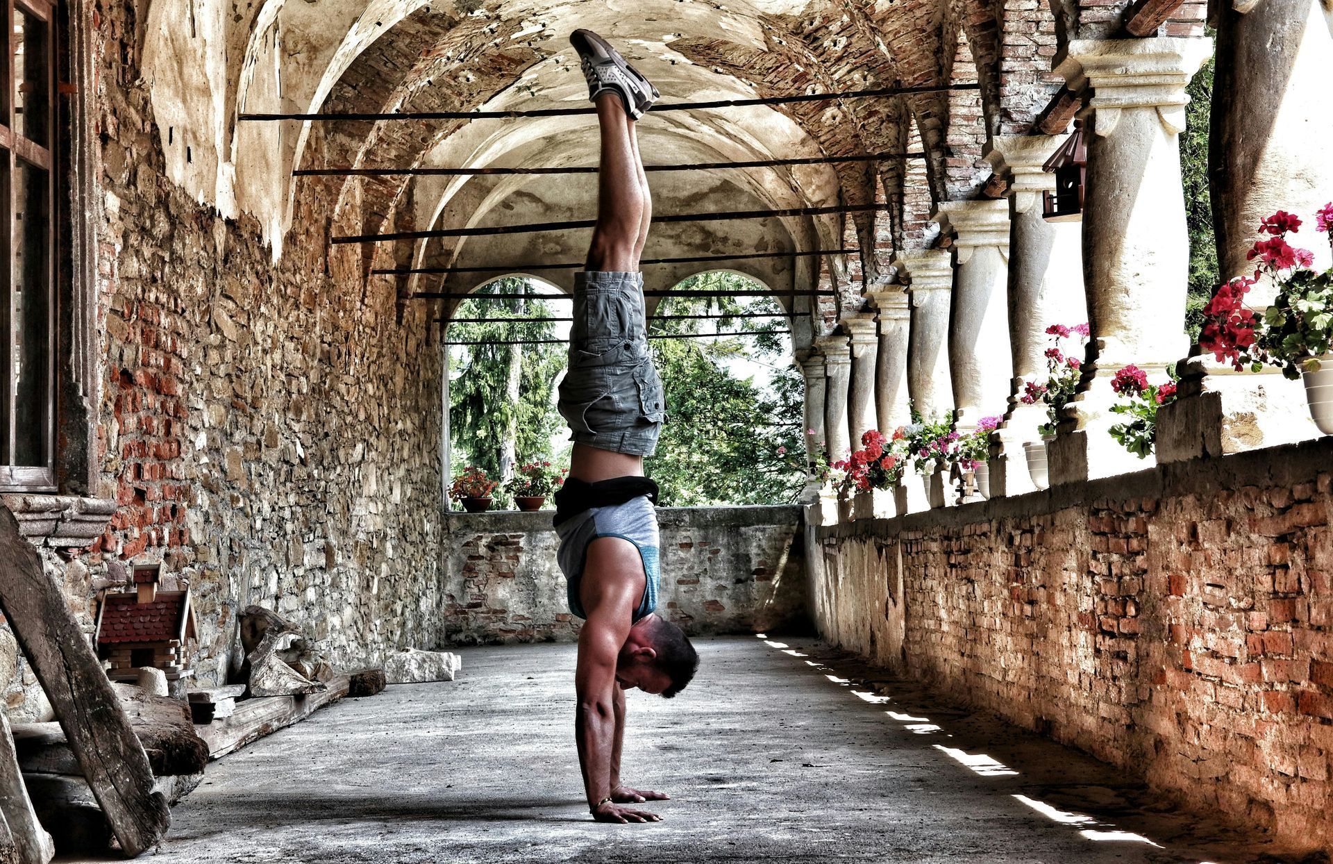 A man is doing a handstand in front of a stone wall.