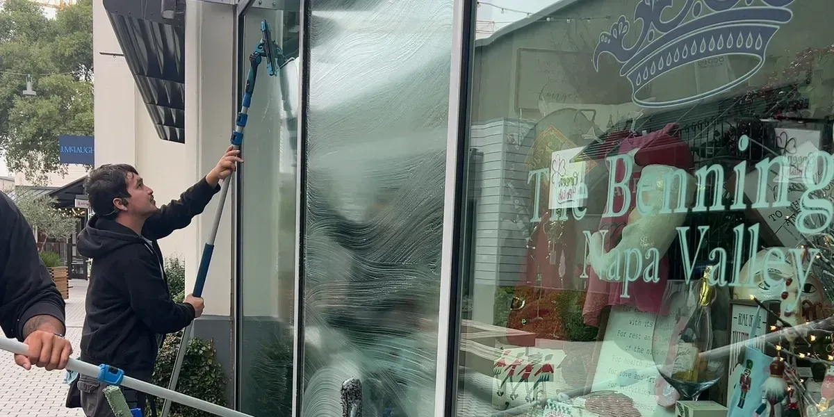 Person washing a large window of a storefront, using a squeegee on a pole.