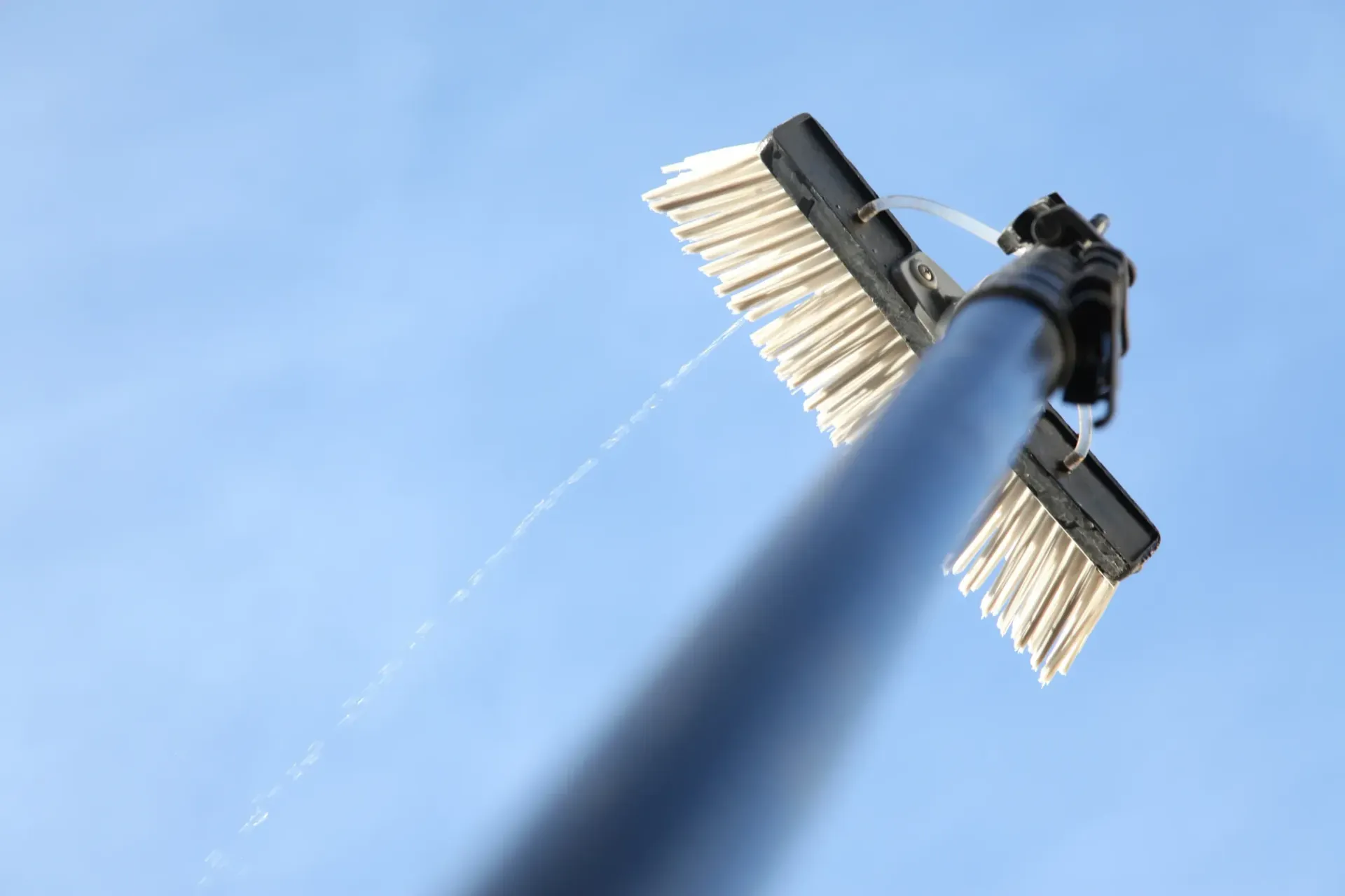 Window cleaning brush spraying water against a blue sky.