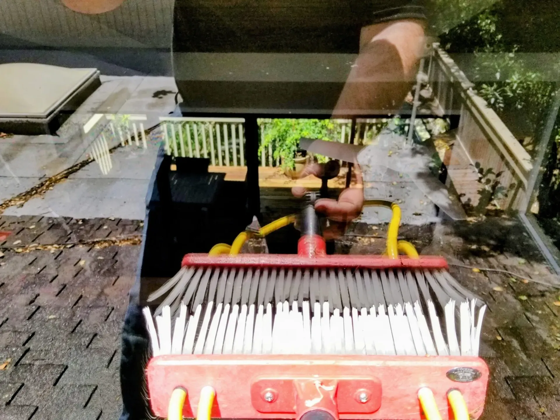 A person cleaning a roof with a brush attached to a pole. A skylight and deck are visible.