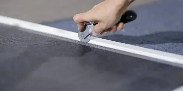 Hand using a tool to trim screen material along a white edge.