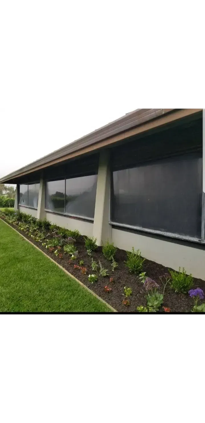 Building with large windows and a brown roof, next to a flowerbed and green lawn.