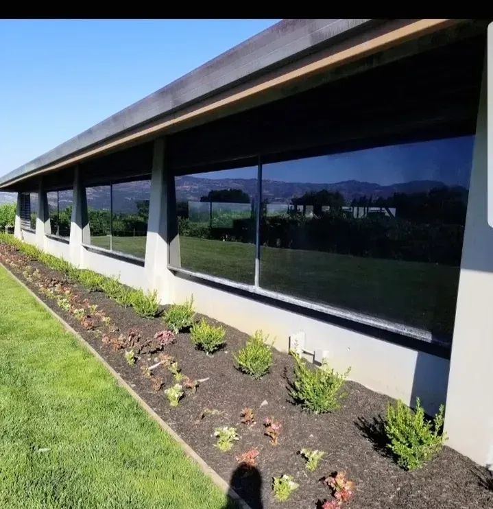 Exterior view of a building with dark tinted windows, a flowerbed, and green lawn under a blue sky.