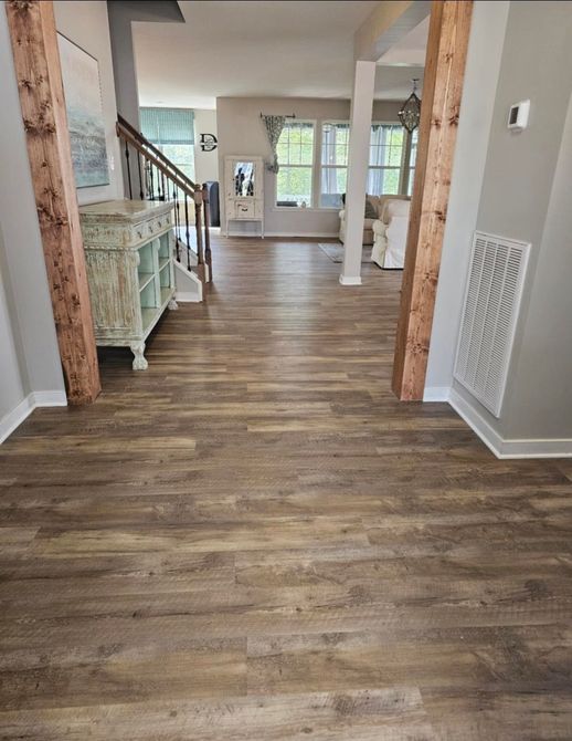Wood-look flooring in a home entrance with wood-beam supports, a light blue cabinet, and a view of the living area.
