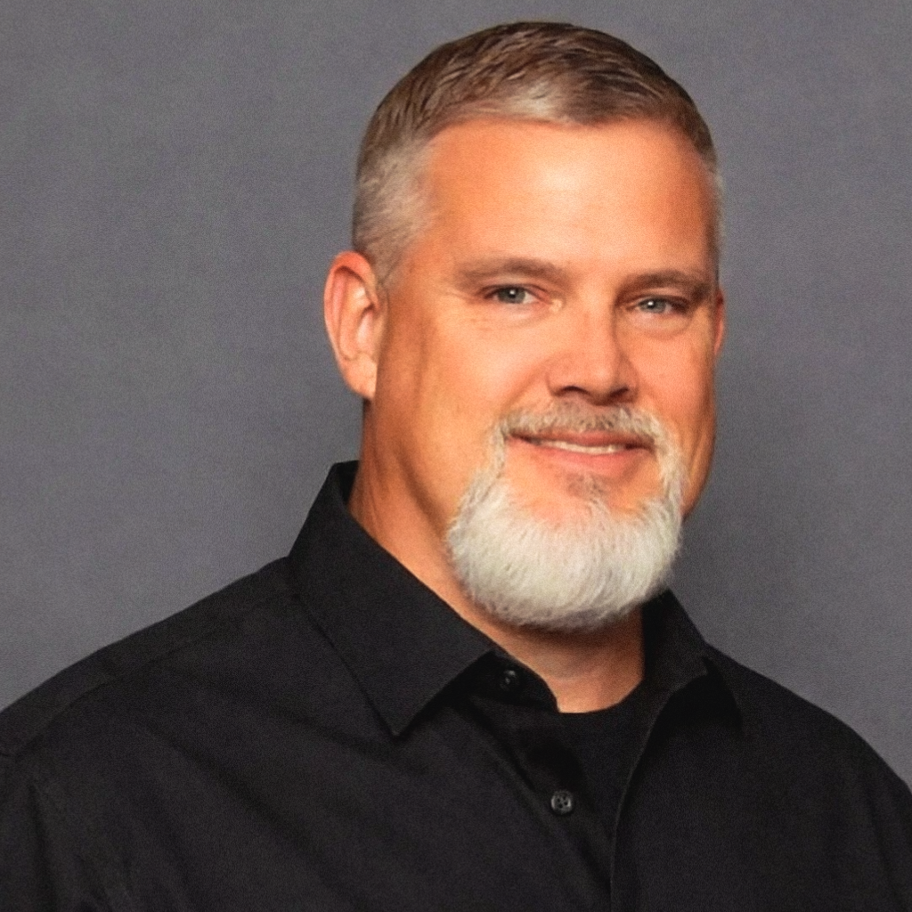 Man with graying hair and beard in vest and tie, smiling.