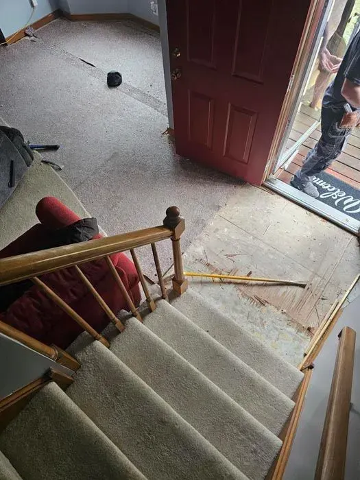 Staircase with carpet leads to an entryway with an open red door. A person stands near the door.