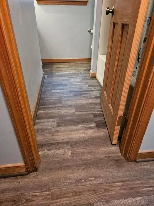 Hallway with wood-look flooring and light blue walls. Ajar wooden door on the right.