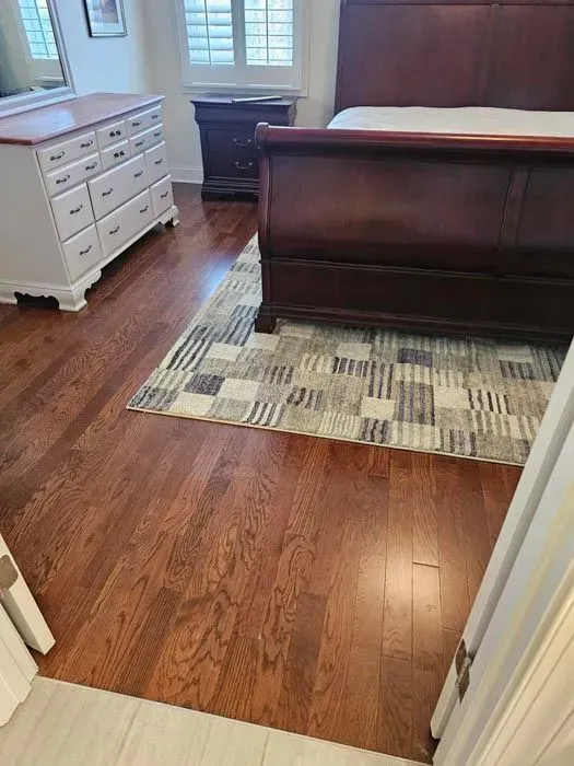 Bedroom with dark wood bed frame, white dresser, and patterned rug on wood flooring.