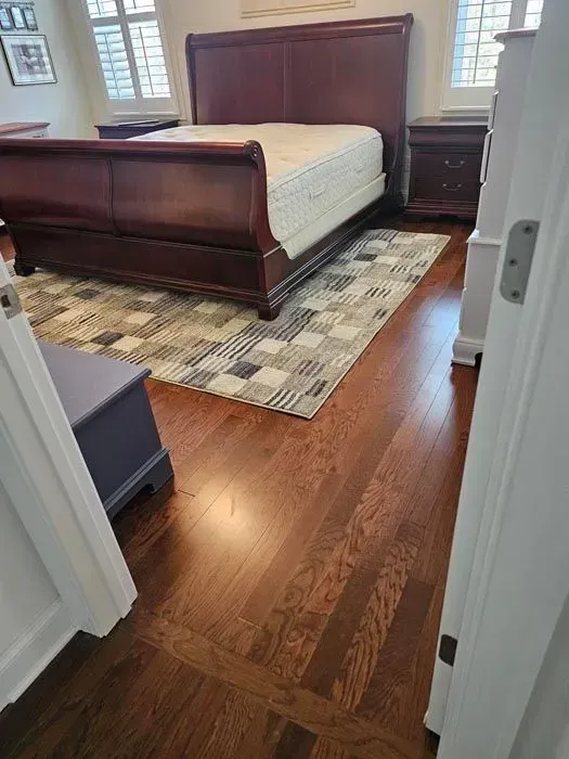 Bedroom with hardwood floors, a dark wooden bed frame, a patterned rug, and furniture.
