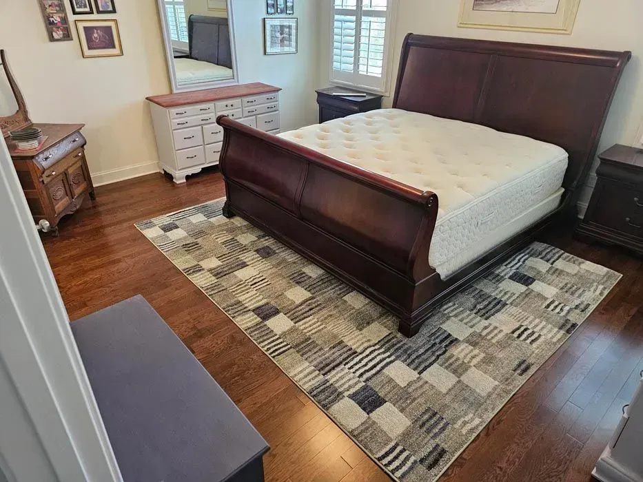 Bedroom with a dark wooden sleigh bed, dresser, and patterned rug on a hardwood floor.