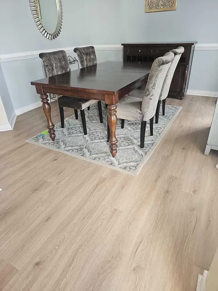 Dining room with a dark wooden table, chairs, rug, and cabinet on light wood-look floor.