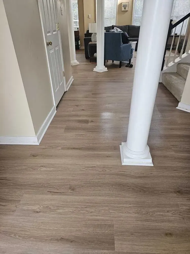 Hallway with light brown wood-look flooring, white pillars, and beige walls.