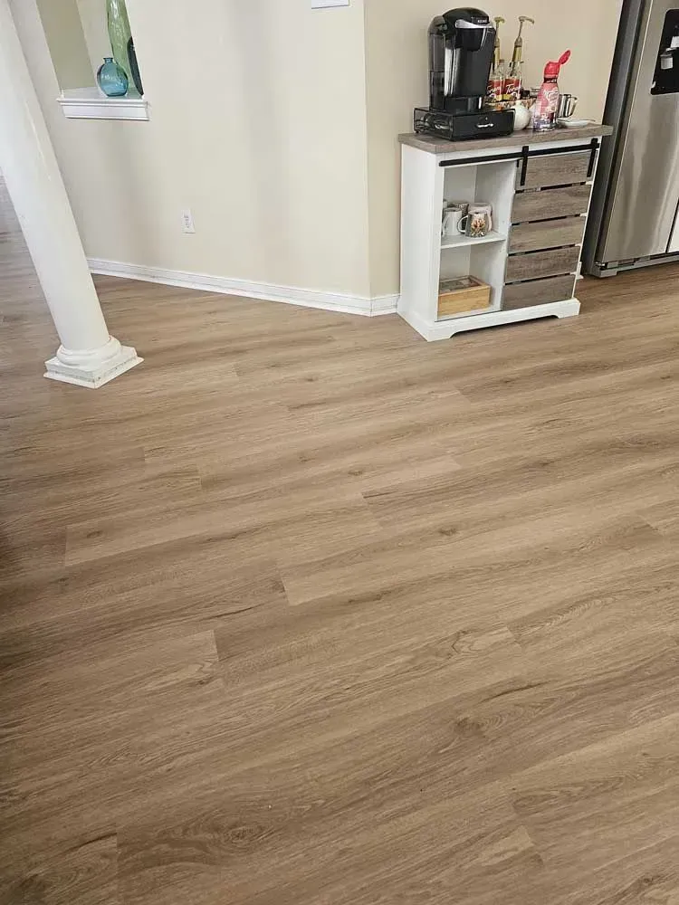 Wooden plank flooring in a room with a white column, coffee station, and cabinets.