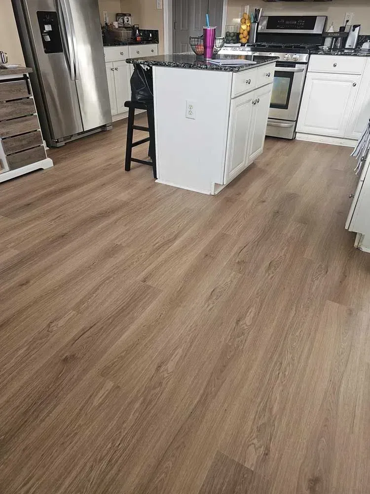Kitchen with wood-look flooring. White cabinets, stainless steel appliances, and an island with a black stool are visible.