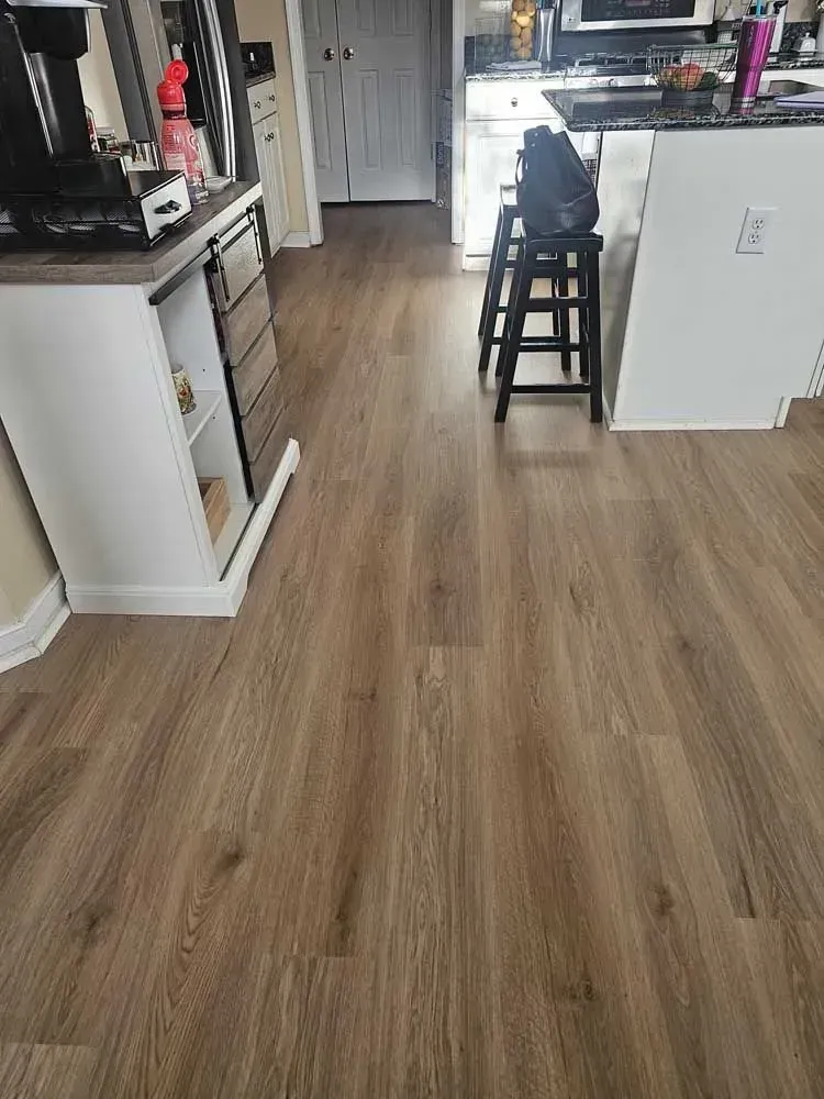 Light brown wood-look flooring extends from kitchen into hallway; a white cabinet, stools, and open door are in view.