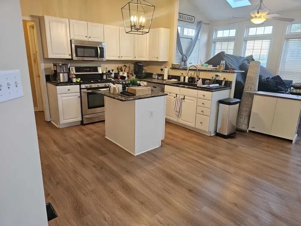 A kitchen with white cabinets, stainless steel appliances, and a wood floor. Island with a black countertop.